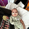 baby, infant, person, oxygen_tube, onesie, medical_equipment, hospital, bed, pillow, hand, face, curious, lying_down, hospital_room, medical_care, purple_wall, red_outlet, blanket, sleepsuit, healthcare