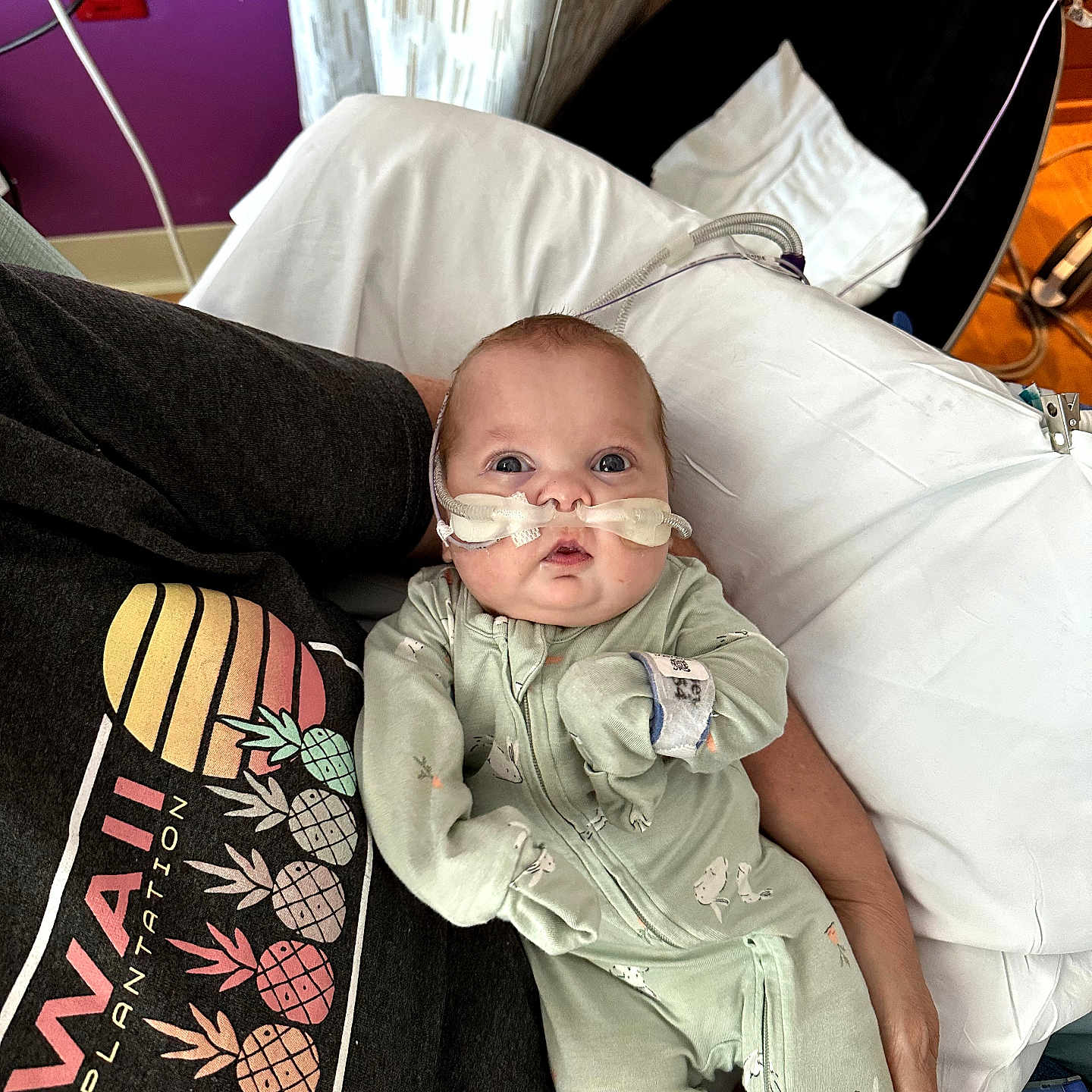 Waylon is registered to the contest to win money with this photo: baby, infant, person, oxygen_tube, onesie, medical_equipment, hospital, bed, pillow, hand, face, curious, lying_down, hospital_room, medical_care, purple_wall, red_outlet, blanket, sleepsuit, healthcare