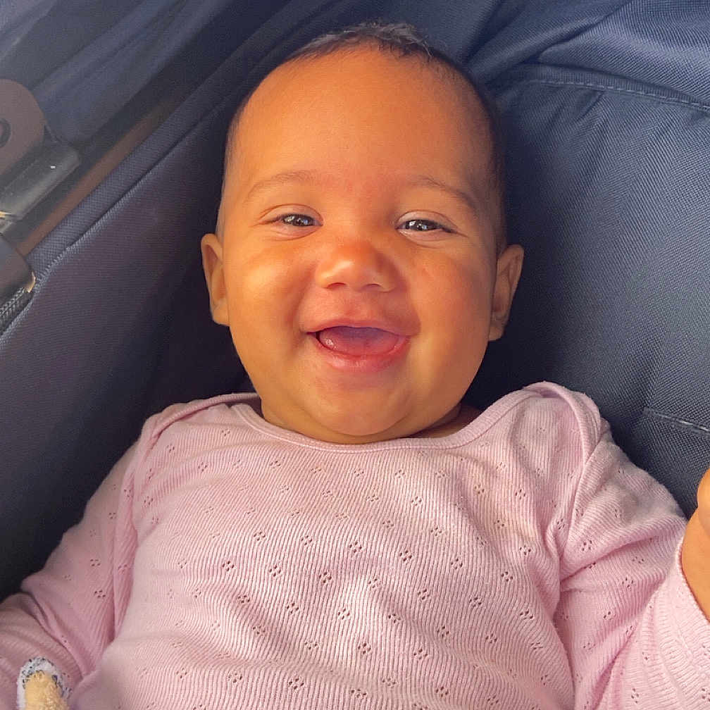 Noëlya participe au concours pour gagner de l'argent avec cette photo : baby, baby_toy, child, clothing, comfort, cozy, cute, face, happy, head, infant, infant_clothing, person, pink_sweater, plush_toy, portrait, seated, smiling, stroller, young_child