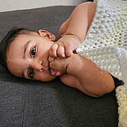 Aariz joined the competition — help win amazing prizes! baby, infant, hand, face, blanket, knitted_blanket, skin, lying_down, curious, eyes, tongue, indoors, closeup, young_child, soft_texture, resting, couch, comfort, small_hand, expression