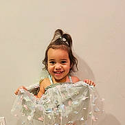 Skylar Rose is registered to the contest to win money with this photo: child, girl, smile, dress, butterfly, hair, topknot, happy, standing, wall, indoor, power_outlet, pastel_colors, fabric, cute, young_child, portrait, holding, playful, fashion