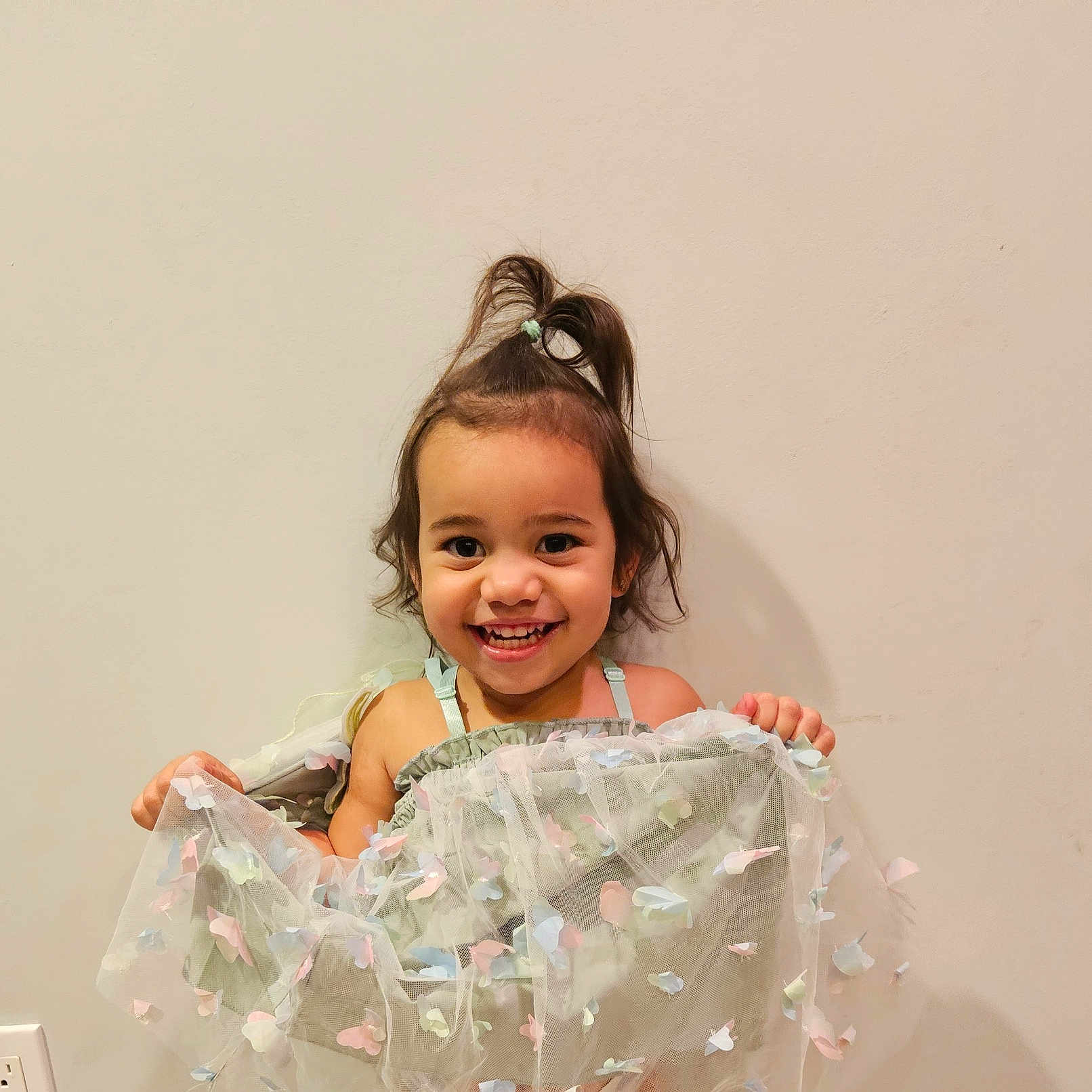 Skylar Rose is registered to the contest to win money with this photo: butterfly, child, cute, dress, fabric, fashion, girl, hair, happy, holding, indoor, pastel_colors, playful, portrait, power_outlet, smile, standing, topknot, wall, young_child