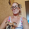 woman, dog, glasses, indoor, portrait, pet, casual, smile, tank_top, brown_dog, face, home_decor, wall, door, necklace, short_hair, looking_at_camera, close_up, sitting, comfortable