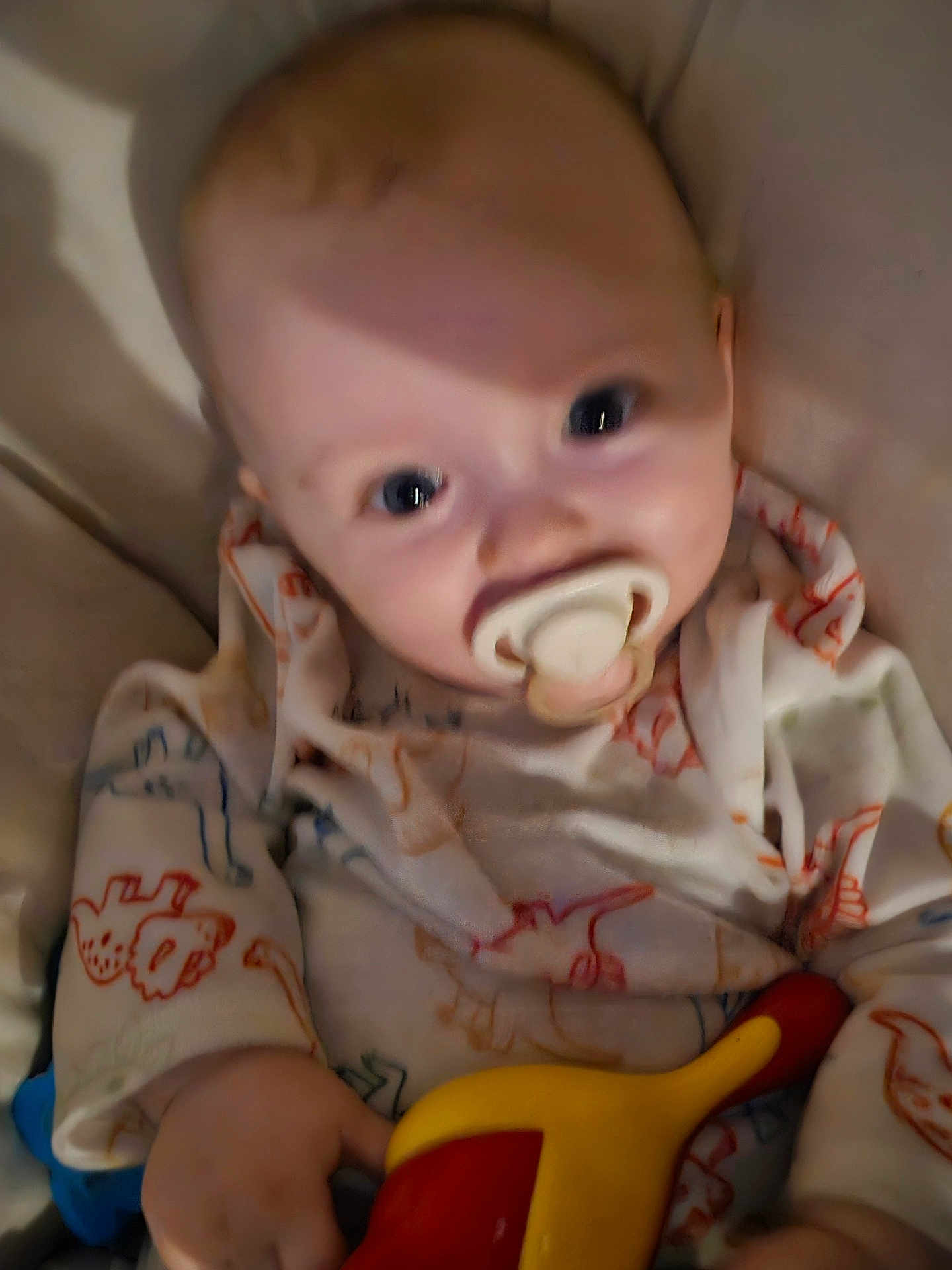 Harrison is registered to the contest to win money with this photo: baby, pacifier, toy, onesie, child, infant, hand, face, closeup, clothing, pattern, colorful, cute, indoors, young, person, soft, blurred, holding, play