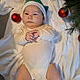 baby, blanket, celebration, christmas, cute, face, festive, green, hands, hat, holiday, indoors, infant, legs, lying_down, onesie, ornament, red, soft_texture, tree_branch