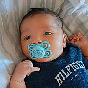 Josué Leonardo is registered to the contest to win money with this photo: baby, pacifier, infant, blue_pacifier, clothing, bed, striped_bed_sheet, hand, face, eyes, cute, lying_down, navy_shirt, hilfiger, child, person, skin, young_child, indoor, portrait