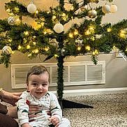 Hamaz Alobaidi joined the competition — help win amazing prizes! baby, child, pajamas, carpet, christmas_tree, ornaments, lights, indoor, holiday, festive, smiling, person, hand, floor, decorations, home, cozy, cheerful, sitting, warm_lighting