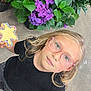 black_shirt, blonde_hair, casual_clothing, child, close_up, concrete_floor, cookie, cute, flower, girl, glasses, greenery, happy, holding, hydrangea, indoor, looking_up, plant_pot, portrait, sprinkles
