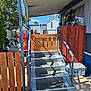 Scrappy Doo is registered to the contest to win money with this photo: blue_sky, concrete, dog, gate, gravel, ladder, lamp, mat, metal_pole, mobile_home, outdoor, plants, plastic_box, porch, railing, shadow, stairs, sunlight, tree, wooden_fence