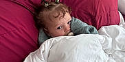 Arrow Saige is registered to the contest to win money with this photo: baby, blanket, bed, bedding, child, curly_hair, cute, face, hair_ties, pacifier, pillow, red_pillow, resting, sleepy, soft, toddler, white_blanket, young_child, indoors, comfort