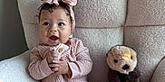 Arrow Saige is registered to the contest to win money with this photo: baby, child, pink_clothing, headband, bow, plush_toy, otter_toy, chair, cozy, knitwear, happy, smiling, indoors, soft_light, couch, toddler, cute, person, seated, furniture