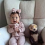 baby, child, pink_clothing, headband, bow, plush_toy, otter_toy, chair, cozy, knitwear, happy, smiling, indoors, soft_light, couch, toddler, cute, person, seated, furniture