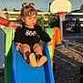 toddler, child, slide, playground, outdoor, basketball_hoop, hand, black_clothing, orange_bows, curly_hair, sunlight, toys, garden, plants, wood_chips, boots, person, daytime, expression, fence