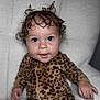 baby, child, curly_hair, leopard_print, onesie, infant, sitting, soft_chair, indoor, cute, portrait, smiling, big_eyes, hand, fingers, young_child, comfortable, white_background, closeup, adorable