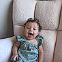 baby, child, curly_hair, blue_outfit, polka_dots, wooden_buttons, flower_clip, happy, smiling, sitting, chair, fluffy_chair, indoor, cute, person, young_child, portrait, comfortable, light_skin, joyful