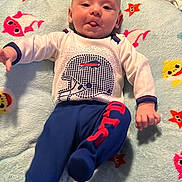 George is registered to the contest to win money with this photo: baby, infant, child, lying_down, blanket, colorful, playful, cute, tongue_out, clothing, long_sleeve, pants, footwear, face, head, expression, indoor, soft_texture, pattern, fun
