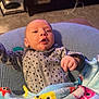 George joined the competition — help win amazing prizes! baby, infant, polka_dot, onesie, blanket, fish_pattern, cushion, living_room, carpet, furniture, face, hand, child, soft_texture, indoor, cute, expression, relaxed, cozy, home