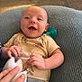 George is registered to the contest to win money with this photo: baby, smiling, pacifier, hand, toy, cushion, knitted, clothing, infant, happy, indoor, person, cute, skin, face, short_sleeve, fabric, comfort, child, relaxing