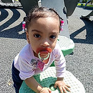 Sevyn joined the competition — help win amazing prizes! blue_pants, child, clothing, curious, daylight, earrings, green_surface, hair_beads, hands, outdoor, pacifier, person, pink_shirt, play_equipment, playground, shadow, sunlight, texture, toddler, young_child