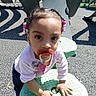 blue_pants, child, clothing, curious, daylight, earrings, green_surface, hair_beads, hands, outdoor, pacifier, person, pink_shirt, play_equipment, playground, shadow, sunlight, texture, toddler, young_child