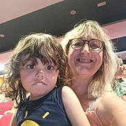 Lazare a rejoint le concours — aidez-le/la à gagner de superbes lots ! child, woman, glasses, curly_hair, indoor, smile, serious_expression, tshirt, yellow_print, person, seated, audience, hair, casual_clothing, portrait, people, red_seat, light, face, happy