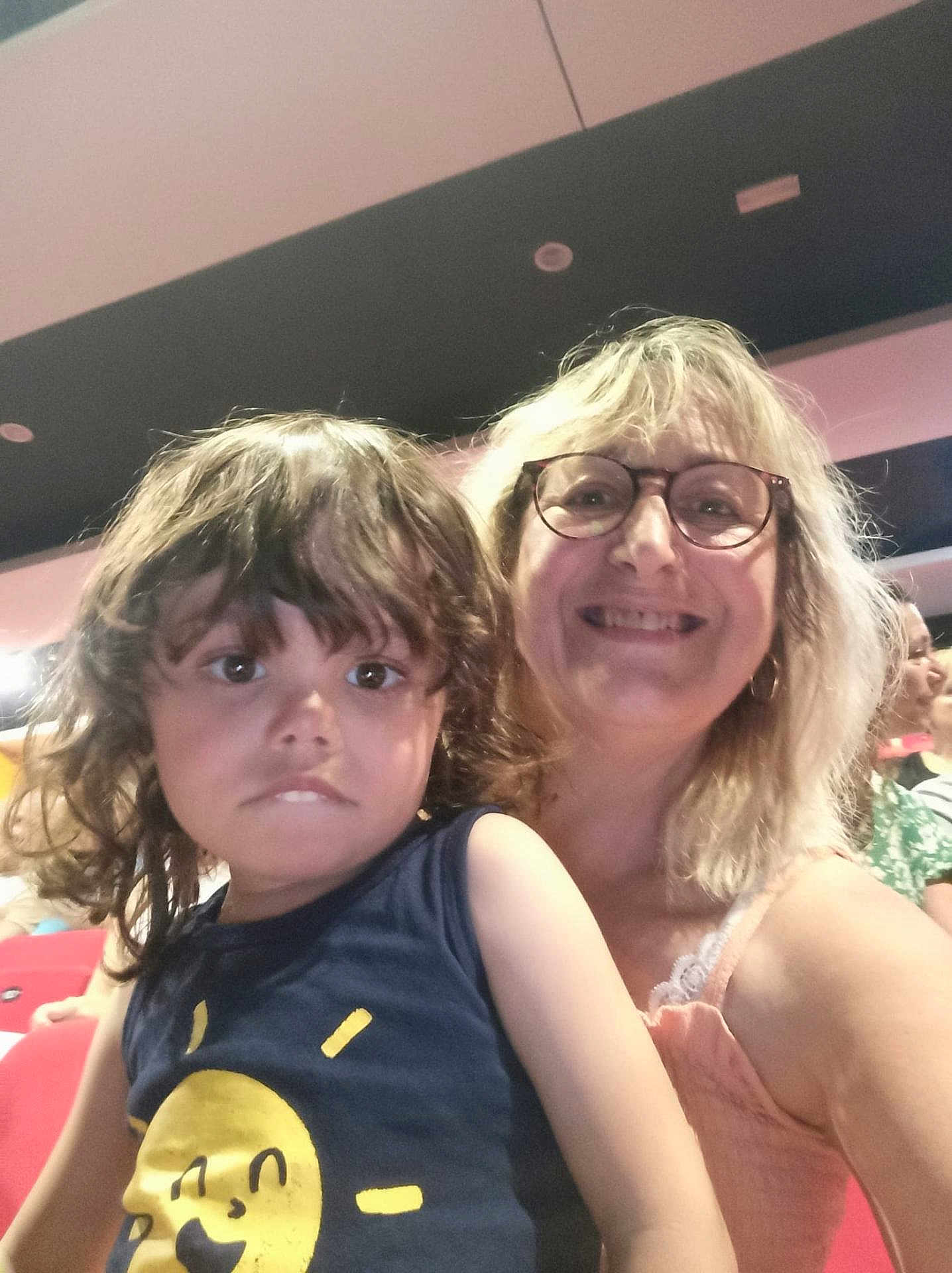 Lazare a rejoint le concours — aidez-le/la à gagner de superbes lots ! child, woman, glasses, curly_hair, indoor, smile, serious_expression, tshirt, yellow_print, person, seated, audience, hair, casual_clothing, portrait, people, red_seat, light, face, happy