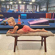 Destiny is registered to the contest to win money with this photo: child, girl, gymnasium, bench, floor, gymnastics, equipment, mats, orange_cone, shorts, black_top, smile, playful, indoor, lighting, person, hair, active, recreation, fun