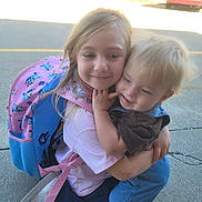 Destiny is registered to the contest to win money with this photo: affection, backpack, blond_hair, candid, casual_clothing, child, children, cute, daylight, friendship, happy, hug, jeans, outdoor, person, playful, shoe, sidewalk, smile, toddler