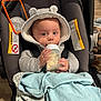Nickolas is registered to the contest to win money with this photo: apparel, baby, blanket, bottle, car_seat, child, clothing, comfort, cute, face, feeding, hand, hooded_sweater, indoor, infant, milk, person, seatbelt, soft, young