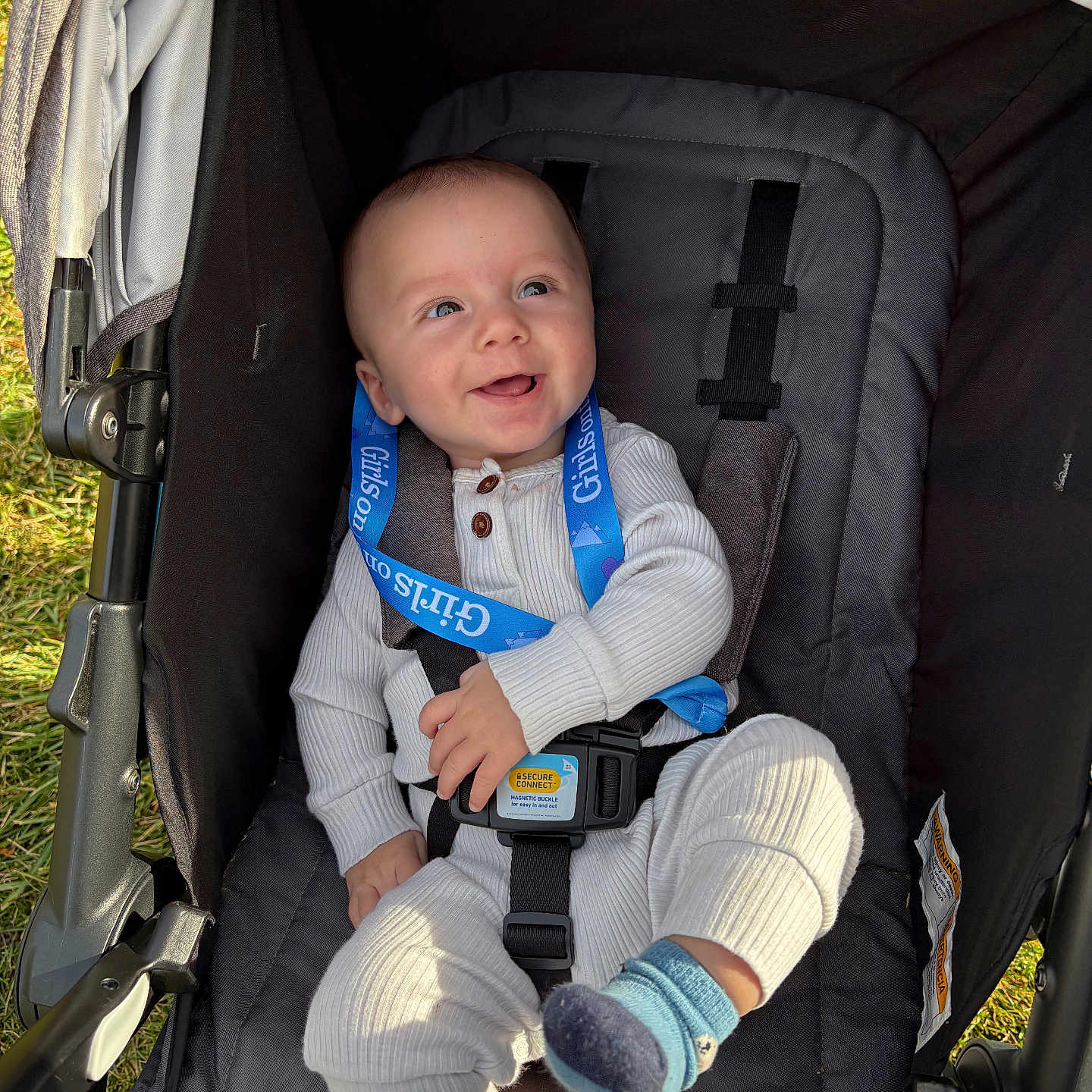 Nickolas is registered to the contest to win money with this photo: baby, baby_shoes, baby_sock, blue_eyes, child, cute, footwear, grass, happy, infant, knitwear, lanyard, outdoor, person, safety_harness, seatbelt, smiling, stroller, sunlight, white_clothing