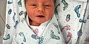 Nickolas is registered to the contest to win money with this photo: newborn, baby, infant, blanket, hospital, crib, swaddled, footprint_pattern, glove, hand, face, hair, cute, wrapped, person, child, indoors, white, blue_glove, pink