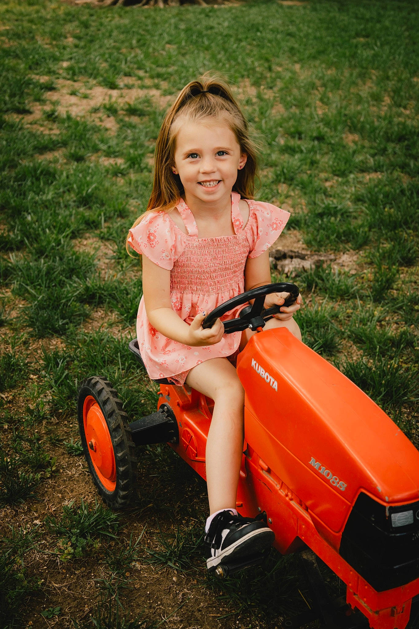 Teagan is registered to the contest to win money with this photo: automotive_design, automotive_lighting, automotive_tire, automotive_wheel_system, blond, child, fender, grass, grassland, happy, joy, motor_vehicle, people_in_nature, person, riding_toy, rim, smile, t_shirt, tire, toddler