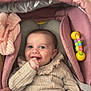 baby, smiling, infant, baby_carrier, pink, knitwear, toy, hand, face, cute, child, portrait, happy, cozy, indoor, clothing, seatbelt, fabric, person, comfort