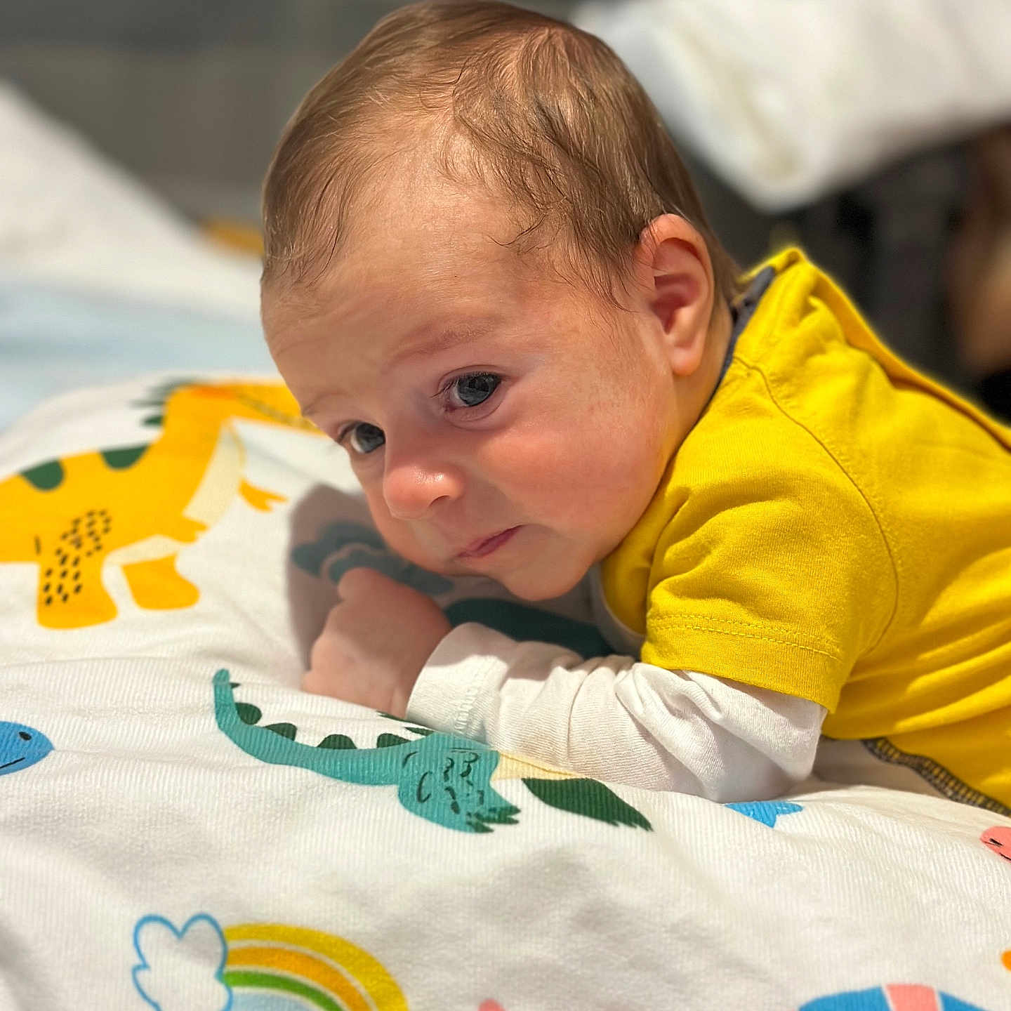 Iannis participe au concours pour gagner de l'argent avec cette photo : baby, bedding, blanket, child, closeup, cozy, cute, dinosaur_pattern, eyes, face, hair, indoor, infant, nursery, portrait, rainbow, skin, sleepy, tummy_time, yellow_shirt