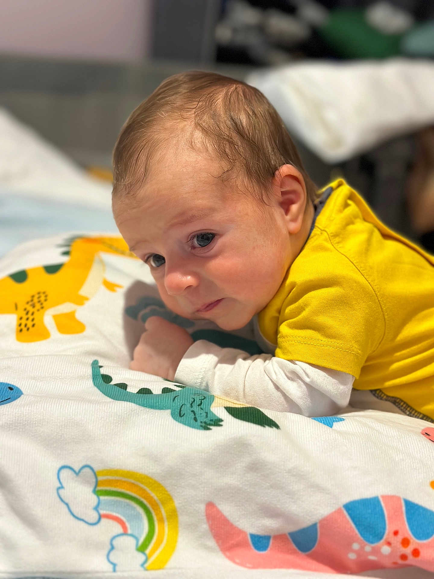 Iannis participe au concours pour gagner de l'argent avec cette photo : baby, infant, child, tummy_time, blanket, yellow_shirt, dinosaur_pattern, rainbow, bedding, portrait, face, eyes, hair, skin, indoor, closeup, sleepy, cute, nursery, cozy