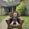Will is registered to the contest to win money with this photo: baby, child, smile, wooden_chair, outdoor, grass, house, pathway, greenery, happy, infant, person, nature, daylight, front_yard, casual_clothing, armrest, feet, head, portrait