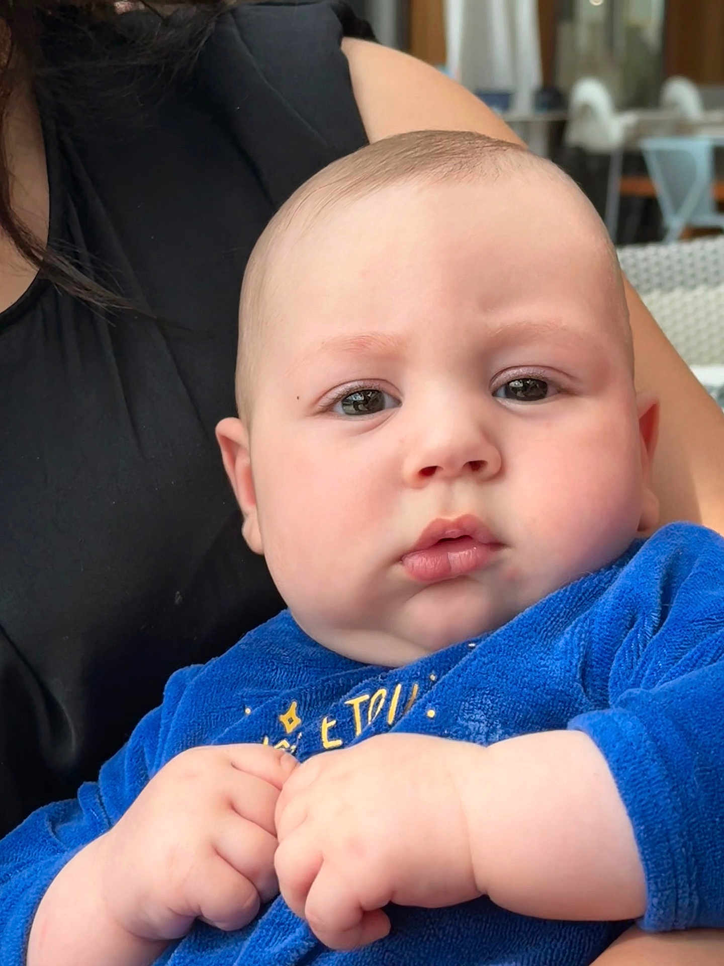 Jed participe au concours pour gagner de l'argent avec cette photo : baby, child, infant, blue_clothing, hands, face, chubby_cheeks, indoor, person, adult, black_clothing, portrait, closeup, curious_expression, skin, human, holding, seated, candid, soft_light