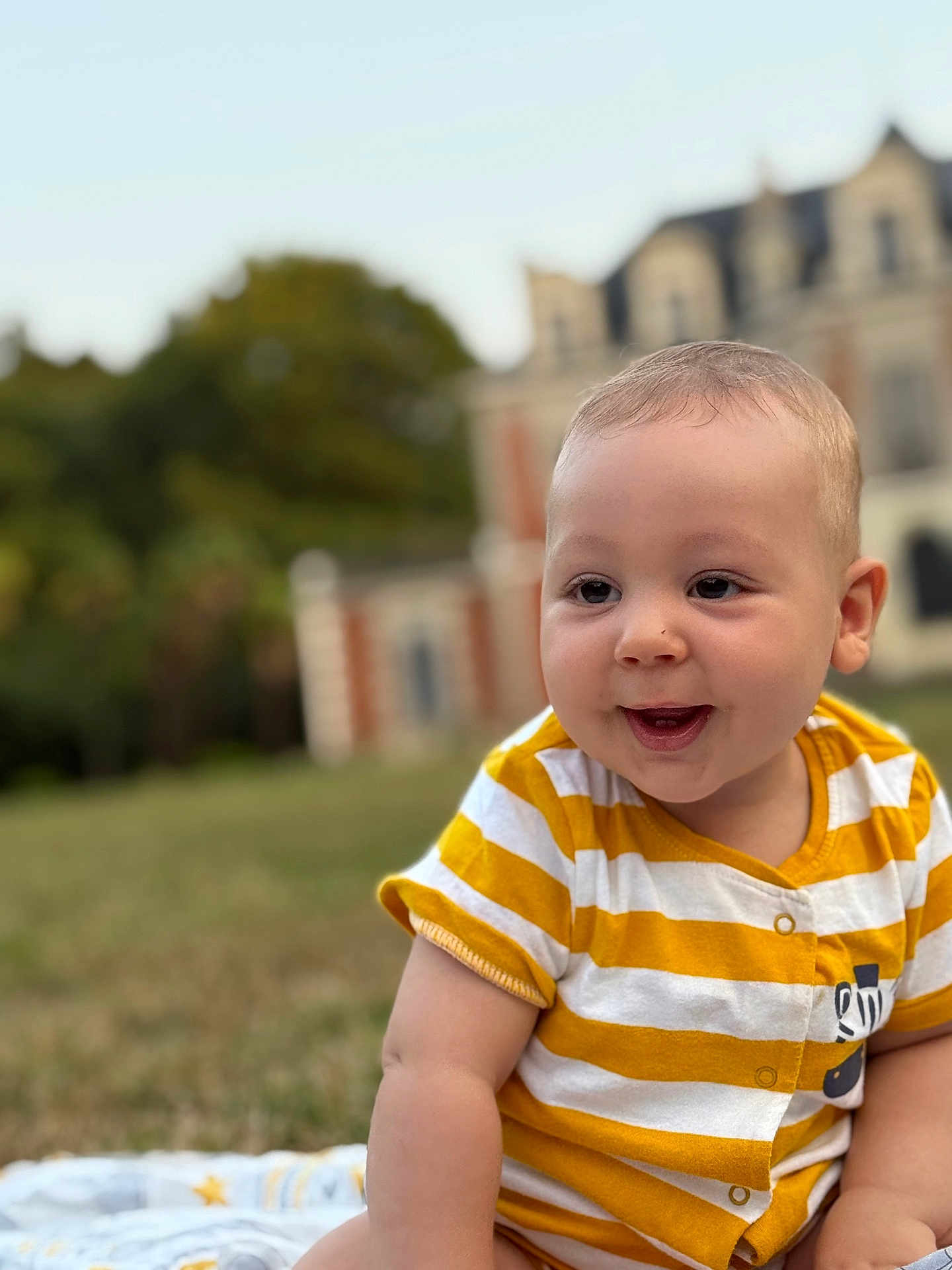 Jed participe au concours pour gagner de l'argent avec cette photo : baby, blanket, blurred_background, building, candid, casual_clothing, child, cute, daylight, face, grass, happy, nature, outdoor, portrait, sitting, smiling, striped_clothing, yellow_shirt, young_child