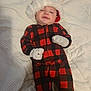 Oliver is registered to the contest to win money with this photo: baby, child, santa_hat, onesie, mittens, sleepy, blanket, plaid, red, black, white, smile, lying_down, indoors, cute, holiday, festive, portrait, infant, cozy