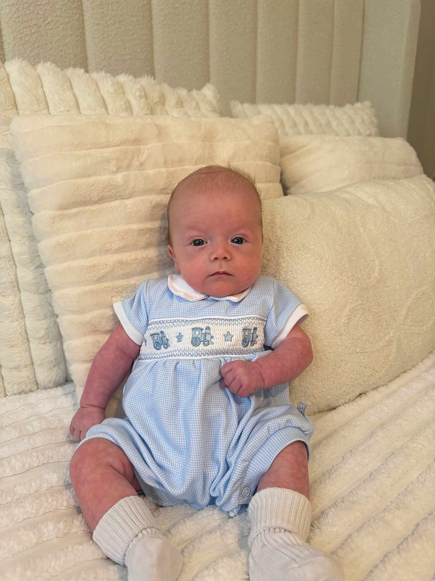 Marley is registered to the contest to win money with this photo: baby, infant, blue_clothing, romper, socks, pillow, blanket, soft_texture, indoor, sitting, cute, child, person, portrait, cozy, comfortable, head, face, expression, resting