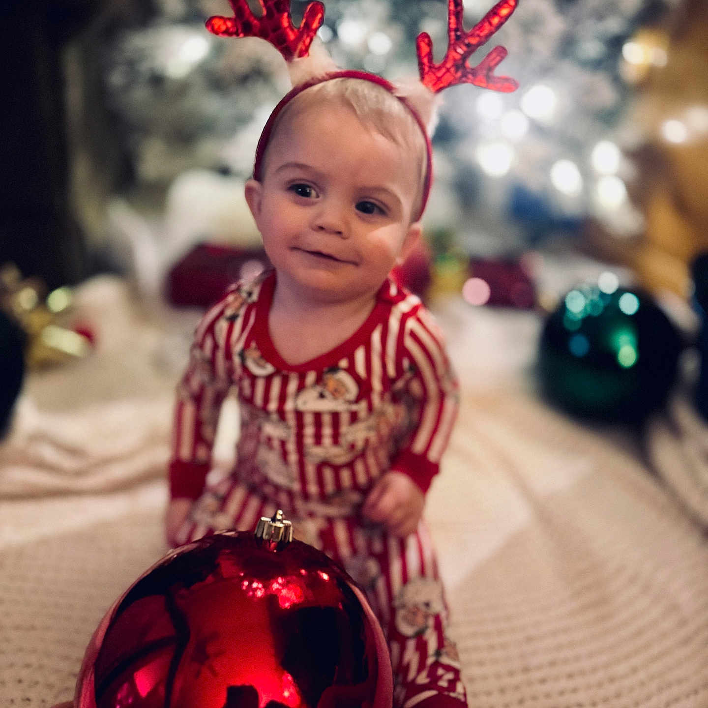 Stephen is registered to the contest to win money with this photo: blanket, celebration, child, christmas, christmas_tree, cute, decorations, festive, holiday, holiday_decor, indoor, lights, ornament, pajamas, red, reindeer_antlers, smile, soft_focus, striped_clothing, toddler