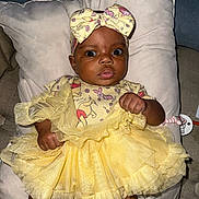 Olympia is registered to the contest to win money with this photo: baby, child, yellow_dress, headband, cushion, pillow, indoors, infant, person, cute, dress, clothing, portrait, sitting, face, hand, expression, looking, fabric, soft