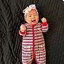 baby, infant, smiling, striped_clothing, onesie, headband, pink_bow, teddy_bear_patch, black_blanket, happy, fists_raised, lying_down, cute, child, portrait, indoors, cheerful, baby_girl, expression, soft_lighting