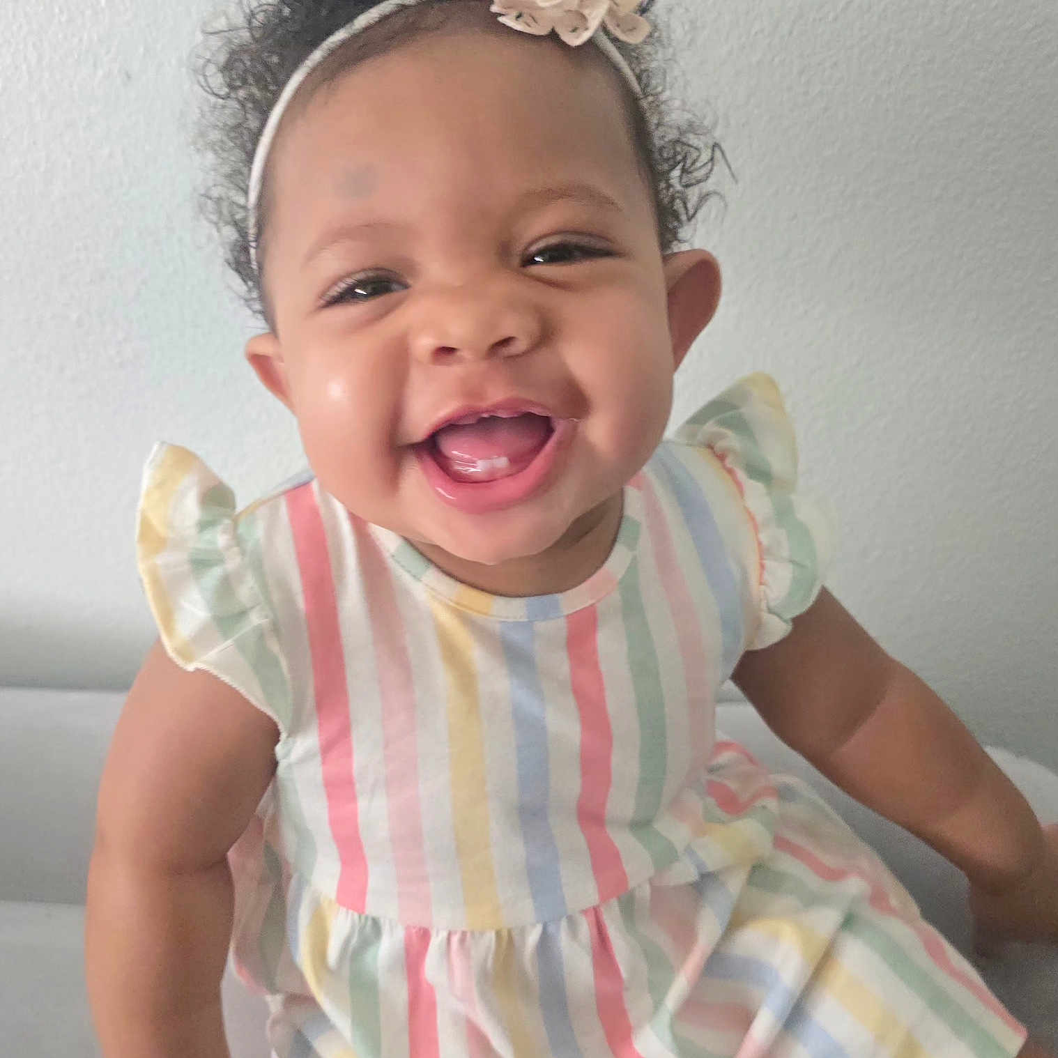 A'Zori joined the competition — help win amazing prizes! baby, child, smile, happy, curly_hair, headband, flower, dress, striped, pastel_colors, ruffle_sleeves, sitting, indoor, light_wall, cute, portrait, person, infant, young_child, joyful