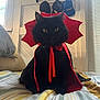 cat, black_cat, costume, cape, red, bed, striped_bedspread, indoor, pet, animal, window, hat_rack, hats, feline, portrait, fur, yellow_eyes, cute, domestic_cat, sitting