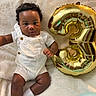baby, child, balloon, number_three, white_overalls, socks, curly_hair, blanket, celebration, indoor, portrait, cute, infant, smiling, skin, person, happy, cozy, soft_texture, lighting