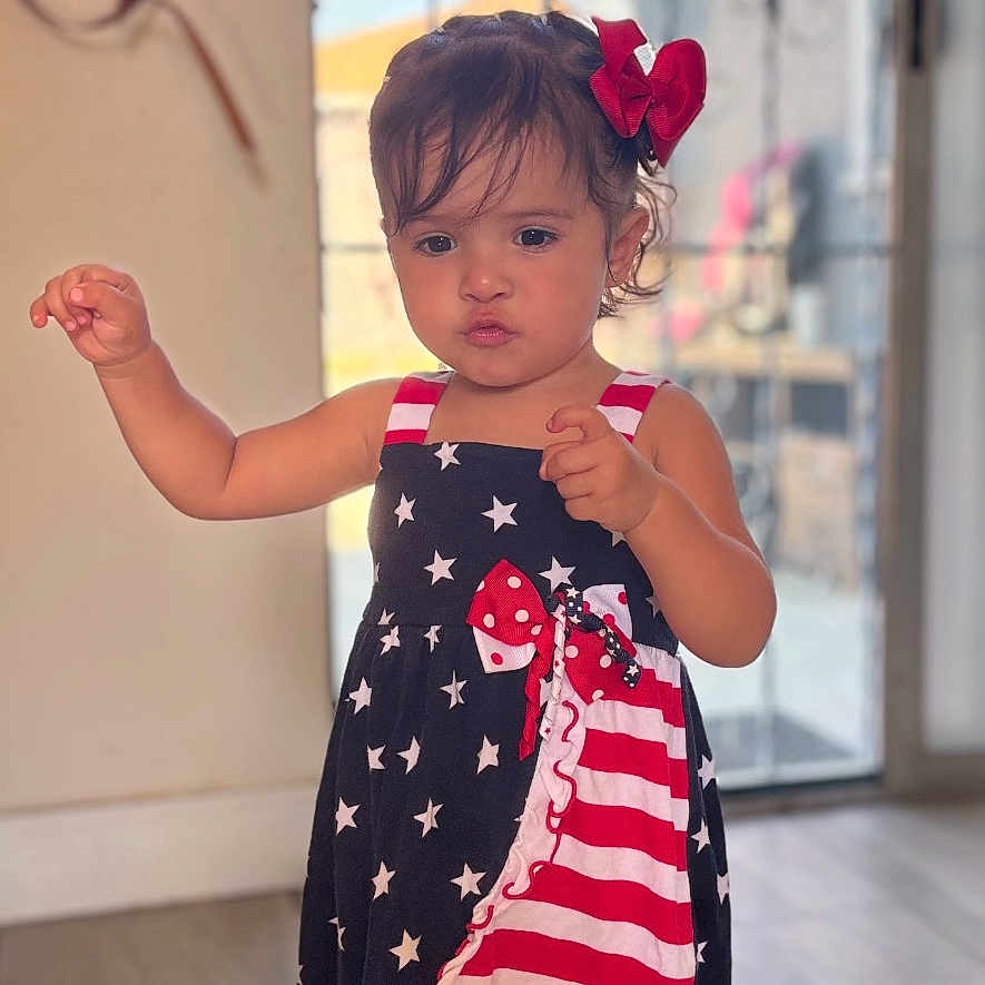 Genavi joined the competition — help win amazing prizes! child, girl, dress, stars, stripes, red_bow, indoor, floor, sandals, curly_hair, pointing, standing, door, window, light, home, portrait, person, cute, fashion