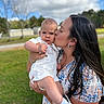 baby, woman, kiss, outdoor, grass, tree, cloud, sky, dress, white_clothing, holding, affection, child, portrait, person, footwear, socks, nature, daylight, love