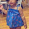 Arya joined the competition — help win amazing prizes! toddler, child, blue_dress, floral_pattern, indoor, wooden_floor, curly_hair, standing, expression, person, furniture, white_chair, flooring, casual, small_object, hand_raised, portrait, cute, young_child, text_overlay