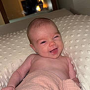 Elianna is registered to the contest to win money with this photo: baby, infant, smile, winking, blanket, pillow, indoor, face, cheerful, skin, head, expression, comfort, lying_down, newborn, home, mirror, soft_texture, wrapped, peaceful